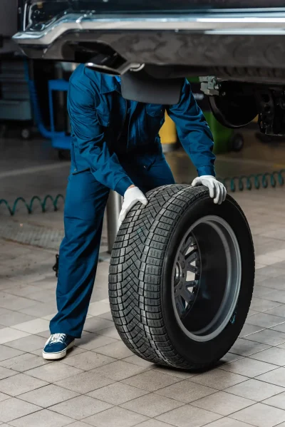 A man rolling a tire and aligning it to the bottom of the car.